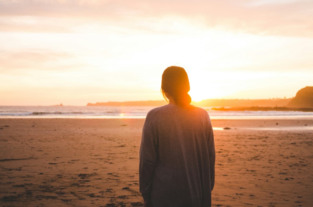 Una donna di spalle, sulla spiaggia al tramonto.